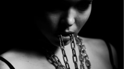  Imagen a blanco y negro de una mujer con cadenas alrededor de su cuello y en su boca.